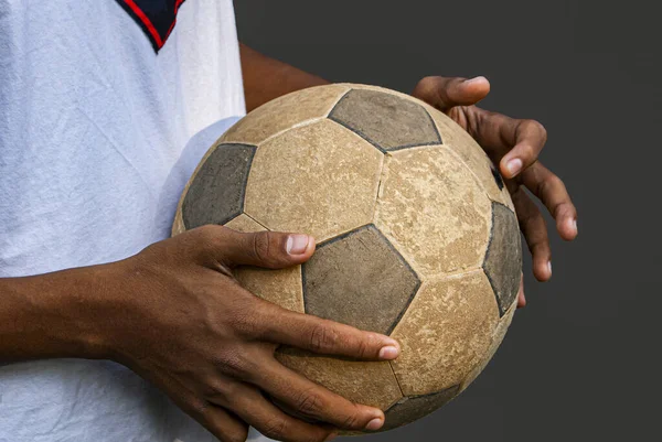 An old football ball in the hands of a child and a gray background