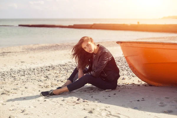 Een meisje zijwaarts in de buurt van een rode boot op het strand door zee — Stockfoto