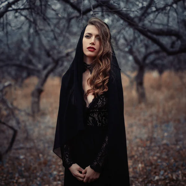 Bella ragazza in abito nero vintage con i capelli ricci in posa nel bosco. Donna in abito retrò perso nella foresta. Emozione sensuale preoccupata. moda retrò — Foto Stock