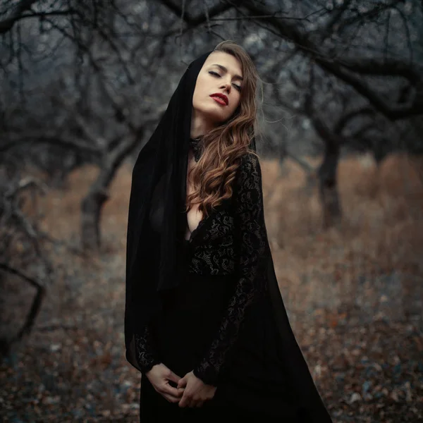 Bella ragazza in abito nero vintage con i capelli ricci in posa nel bosco. Donna in abito retrò perso nella foresta. Emozione sensuale preoccupata. moda retrò — Foto Stock