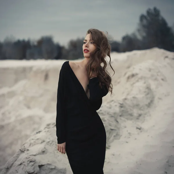 Hermosa chica en vestido vintage negro con el pelo rizado posando en la arena. Mujer en retro dres. Emoción sensual preocupada. Moda retro . — Foto de Stock