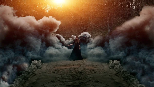 Young attractive Witch walking on the bridge in heavy black smoke. — Stock Photo, Image