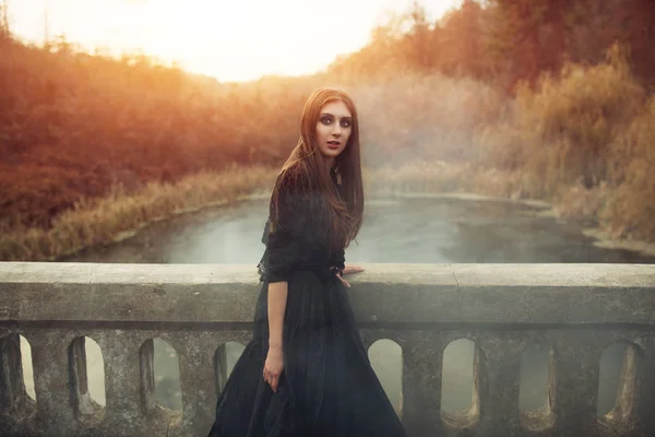 Giovane strega attraente che cammina sul ponte in fumo nero pesante . — Foto Stock