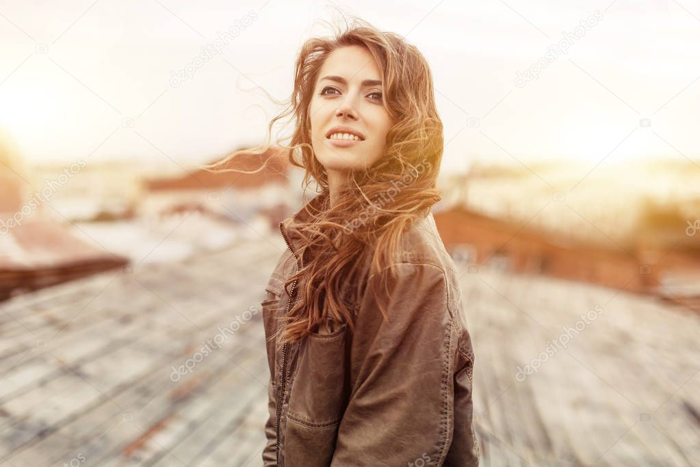 Young attractive woman with good mood enjoying beautiful city landscape while standing on a roof of building, charming smiling hipster girl relaxing after excursion during her amazing spring weekend