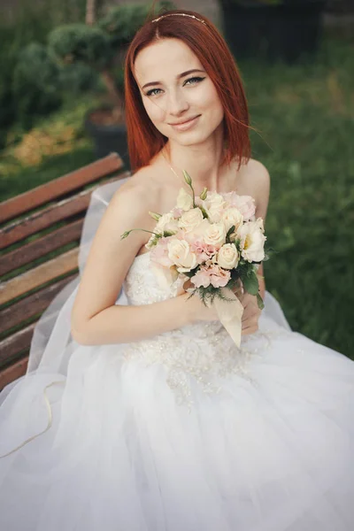 Bride in elegant wedding gown sits on stone bench — Stock Photo, Image