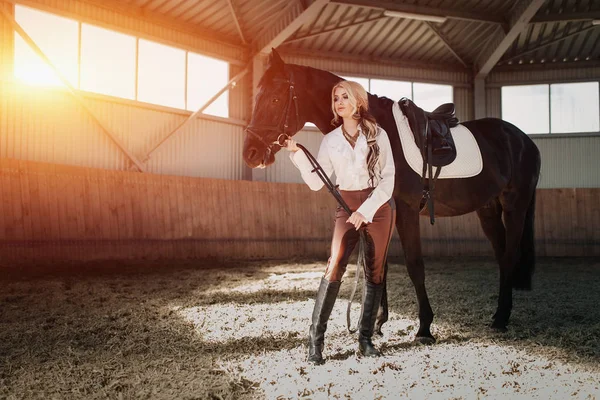 Linda menina loira elegante de pé perto de seu cavalo vestir competição uniforme — Fotografia de Stock