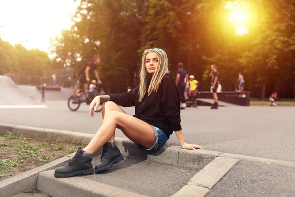 Bonita jovem mulher fitness com capuz preto sentado perto do parque de skate . — Fotografia de Stock