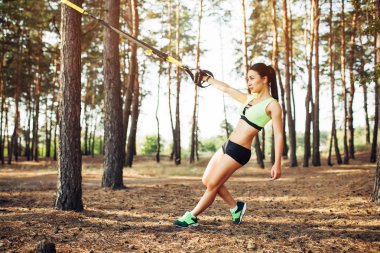 Süspansiyon antrenörle trx egzersiz yaparak güzel genç kadın