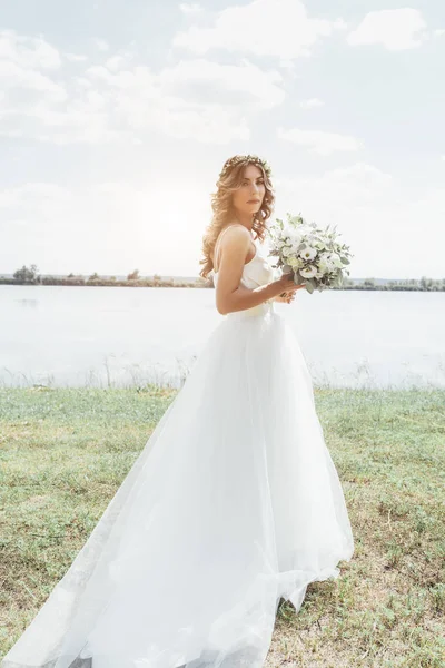 Noiva em um vestido branco de pé segurando um buquê de casamento de flo — Fotografia de Stock