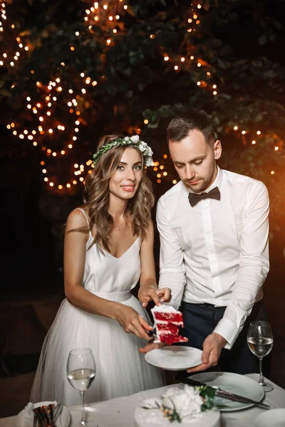 A noiva vestida de branco e noivo cortar o bolo de casamento sob a la — Fotografia de Stock