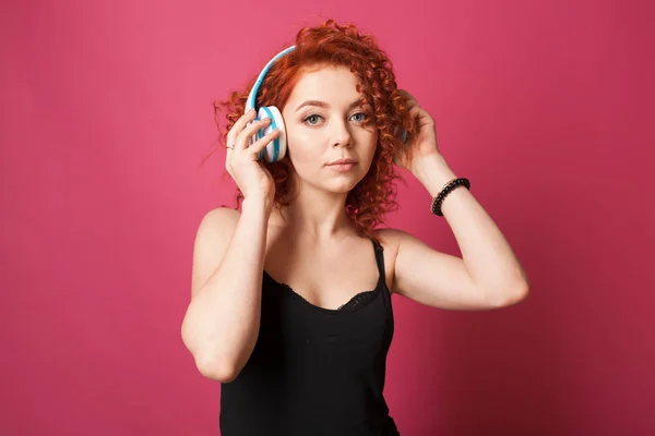 Curly redhead girl listens to music with headphones. Studio — Stock Photo, Image