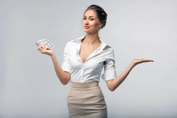Schöne europäische Geschäftsfrau in Bürokleidung hält Dollars in der rechten Hand und hält ihre linke Hand offen — Stockfoto
