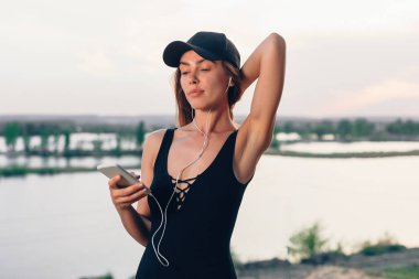 Kadın fitness egzersiz üzerinde çalışan kablosuz kulaklıkları. Aktif yaşam tarzı atlet smartphone müzik telefonu uygulaması ile kulak içi dişli plajda dinlerken.