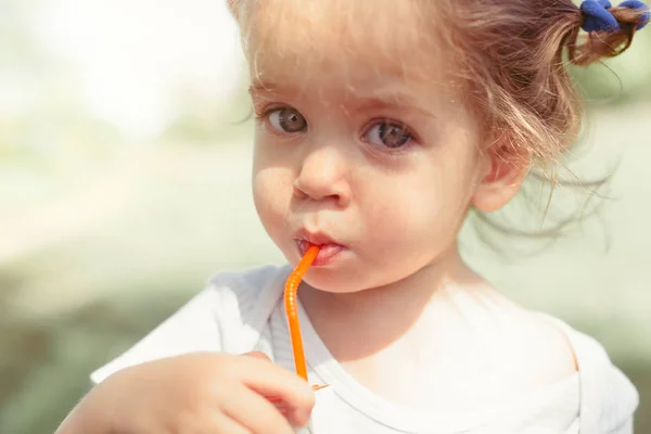 Soliga porträtt av ett litet barn som dricker från en halm juiceon suddig sommaren bakgrund — Stockfoto