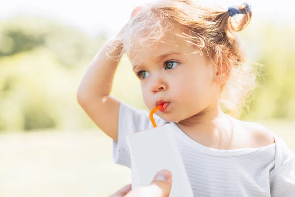 Zonnig portret van een klein kind drinken uit een rietje juiceon zomer achtergrond wazig — Stockfoto