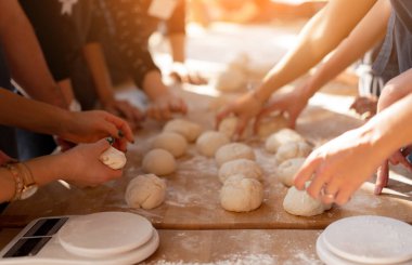 Üretim sırasında ahşap bir masada çörek pişirmek için hamur topları oluşturan yakın plan eller. Aşçılık yüksek lisans sınıfları