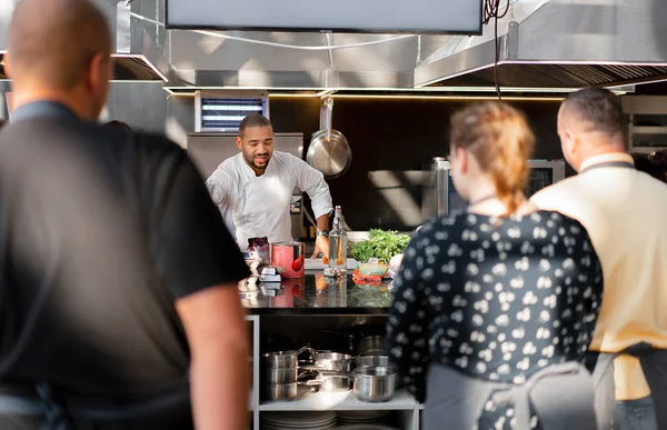 En el foco está el chef que lleva a cabo una clase magistral en la cocina. En primer plano hay imágenes borrosas de personas de atrás observando el proceso. — Foto de Stock