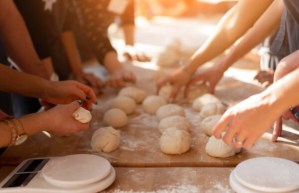 Close-up hands forming dough balls for baking buns on a wooden table during manufacture. Culinary master classes
