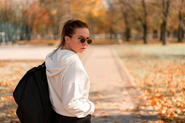 A young beautiful woman with a ponytail and sunglasses, with a backpack on his shoulders in the park. Photo from the back — Stock Photo, Image