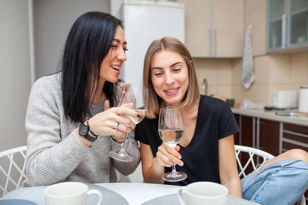 Friends meeting with wine and cake in the modern style kitchen. Young women smile and joke with glasses of wine in his hands