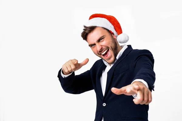 Jovem cara caucasiano bonito em terno de negócios e chapéus de Papai Noel fica no fundo branco em estúdio smilie e mostrando Dedo para a câmera . — Fotografia de Stock