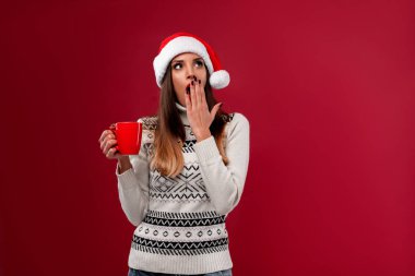 Kırmızı stüdyo arka planında kırmızı Noel Baba şapkalı güzel beyaz kadın. Noel ve Yeni Yıl tatili konsepti.