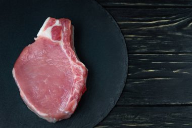 Siyah bir taş kesme tahtası üzerinde bir adet çiğ domuz pirzolası biftek üst görünümü.