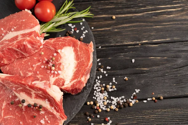 Drei saftige rohe Rindfleischstücke auf einem Steinschneidebrett auf schwarzem Holztischhintergrund. — Stockfoto