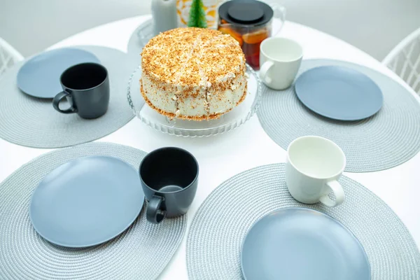 White biscuit cake cut on a stand on a serving table. Around the cake lay out plates with cups and tea — Stock Photo, Image