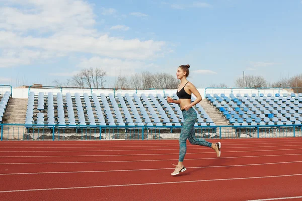 Mujer joven corriendo durante la mañana soleada en pista de estadio — Foto de Stock