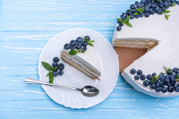 Appetizing cheesecake cake biscuit pillow decorated white cream blueberries and mint stands on wooden blue rustic table — Stock Photo, Image