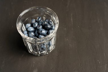 Koyu siyah beton arka plan üzerinde şeffaf bir cam fincan ile güzel lezzetli ham yaban mersini.