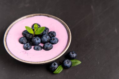 Siyah koyu masa arka planda duran seramik kase lezzetli taze yaban mersini yoğurt sallamak tatlı. 