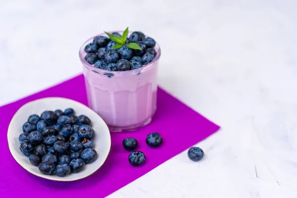 Sabroso yogur de arándano fresco agitar postre en vidrio de pie sobre fondo de servilleta púrpura mesa blanca . — Foto de Stock