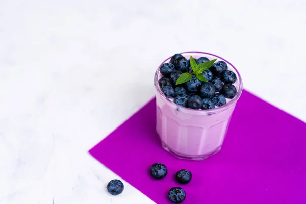 Sabroso yogur de arándano fresco agitar postre en vidrio de pie sobre fondo de servilleta púrpura mesa blanca . — Foto de Stock
