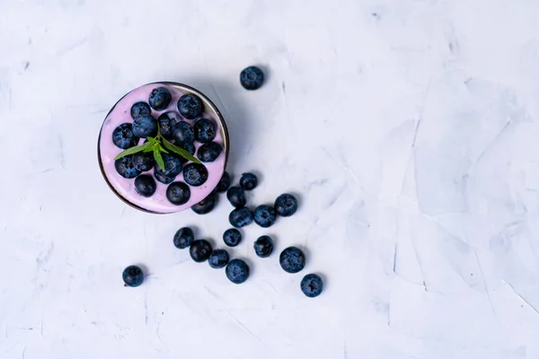 Sabroso postre fresco del batido del yogur del arándano en el tazón de cerámica parado en fondo blanco de la tabla . — Foto de Stock