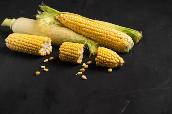 Corn cob with green leaves lies on table black color background. — Stock Photo, Image