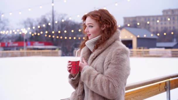 Junge schöne rothaarige Mädchen Sommersprossen Eisbahn auf dem Hintergrund. Hübsche Frau mit lockigem Haar Porträt zu Fuß auf Neujahrsmesse. — Stockvideo