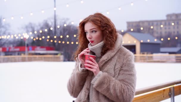 Jovem linda ruiva menina sardas pista de gelo no fundo. Mulher bonita cabelo encaracolado retrato andando na feira de ano novo. — Vídeo de Stock