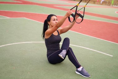 Kız atlet spor alanında egzersiz yapıyor. Melez ırktan genç bir kadın süspansiyon sistemiyle egzersiz yapıyor. Sağlıklı bir yaşam tarzı. Açık havada oyun parkına uzanmak.