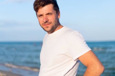 Caucasian man standing on the sea beach dressing white shirt
