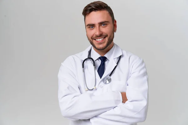 Joven guapo médico moderno en un vestido médico blanco se encuentra en el estudio sobre un fondo blanco. Estudiante en prácticas de una universidad médica . — Foto de Stock