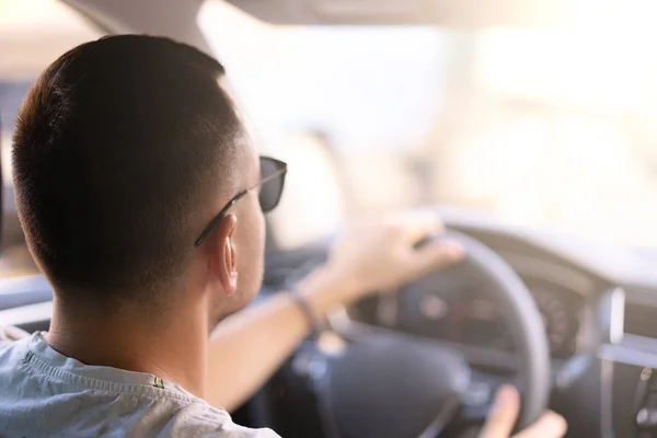 Joven hombre caucásico sentado en un coche vista trasera sosteniendo el volante; viendo la traducción en un día soleado brillante — Foto de Stock