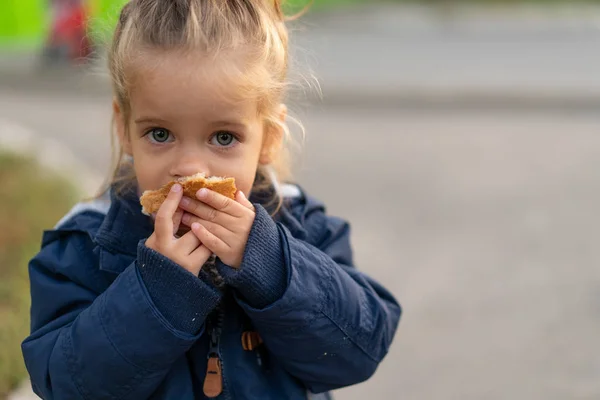 Een prachtig blank meisje met blond haar en gretig brood etend met haar handen kijkt met droevige ogen naar de camera — Stockfoto