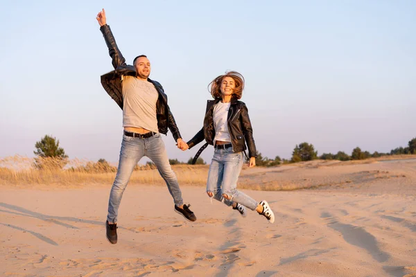 Молодая красивая кавказская пара, прыгающие мужчина и женщина, держась за руки на песчаном пляже . — стоковое фото