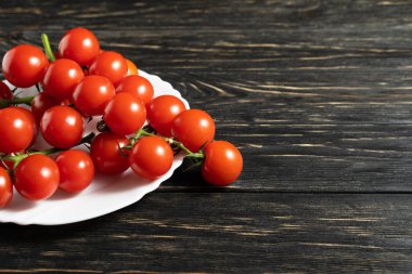 Ahşap masa üzerinde beyaz tabakta kiraz domates