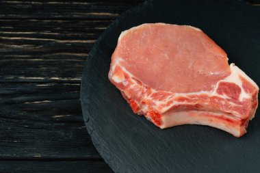 Siyah bir taş kesme tahtası üzerinde bir adet çiğ domuz pirzolası biftek üst görünümü.