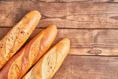 Three crispy french baguettes lie on an old wooden table with free space for text
