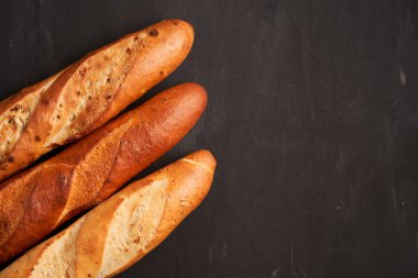 Three crispy french baguettes lie on an old wooden table with free space for text