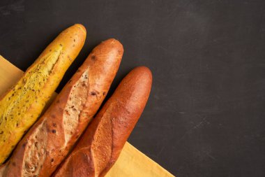 Three crispy french baguettes lie on an old wooden table with free space for text
